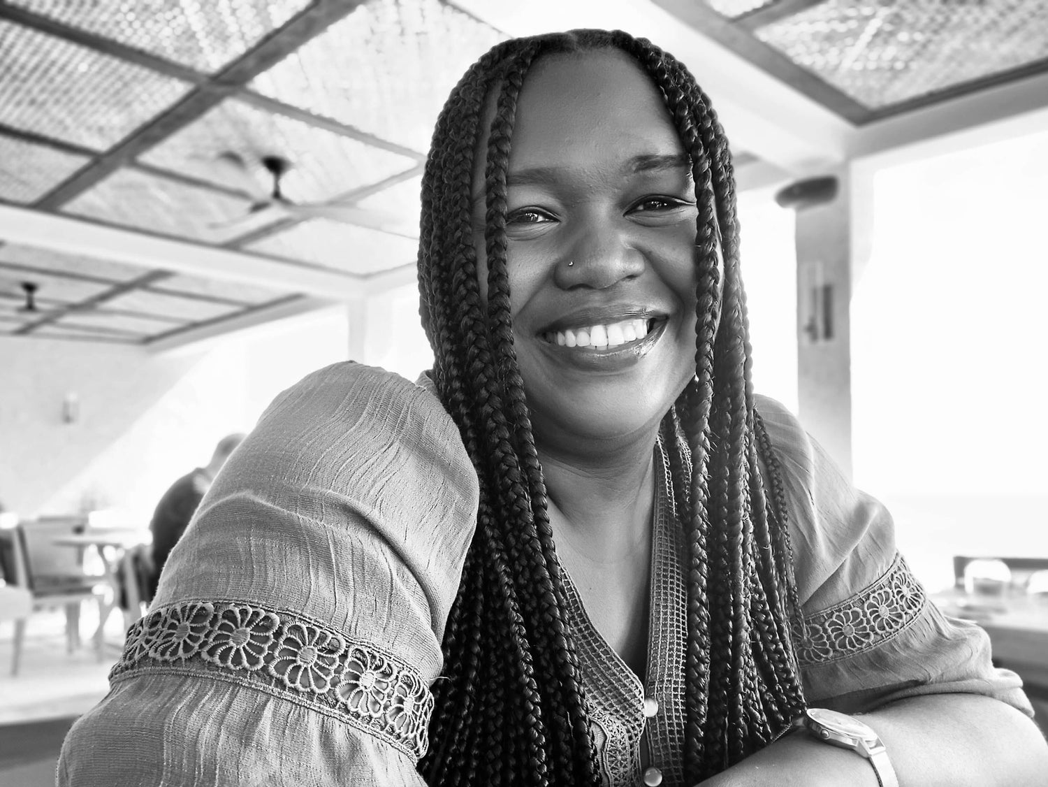 Black and white photo of a woman with braided hair smiling indoors.